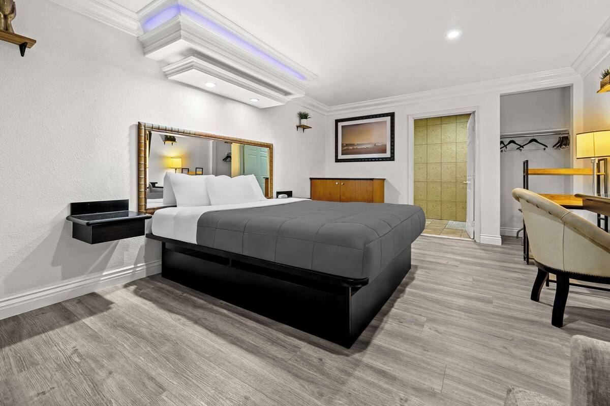 A modern hotel room with a large bed, a bedside table, a chair, and a wardrobe.
