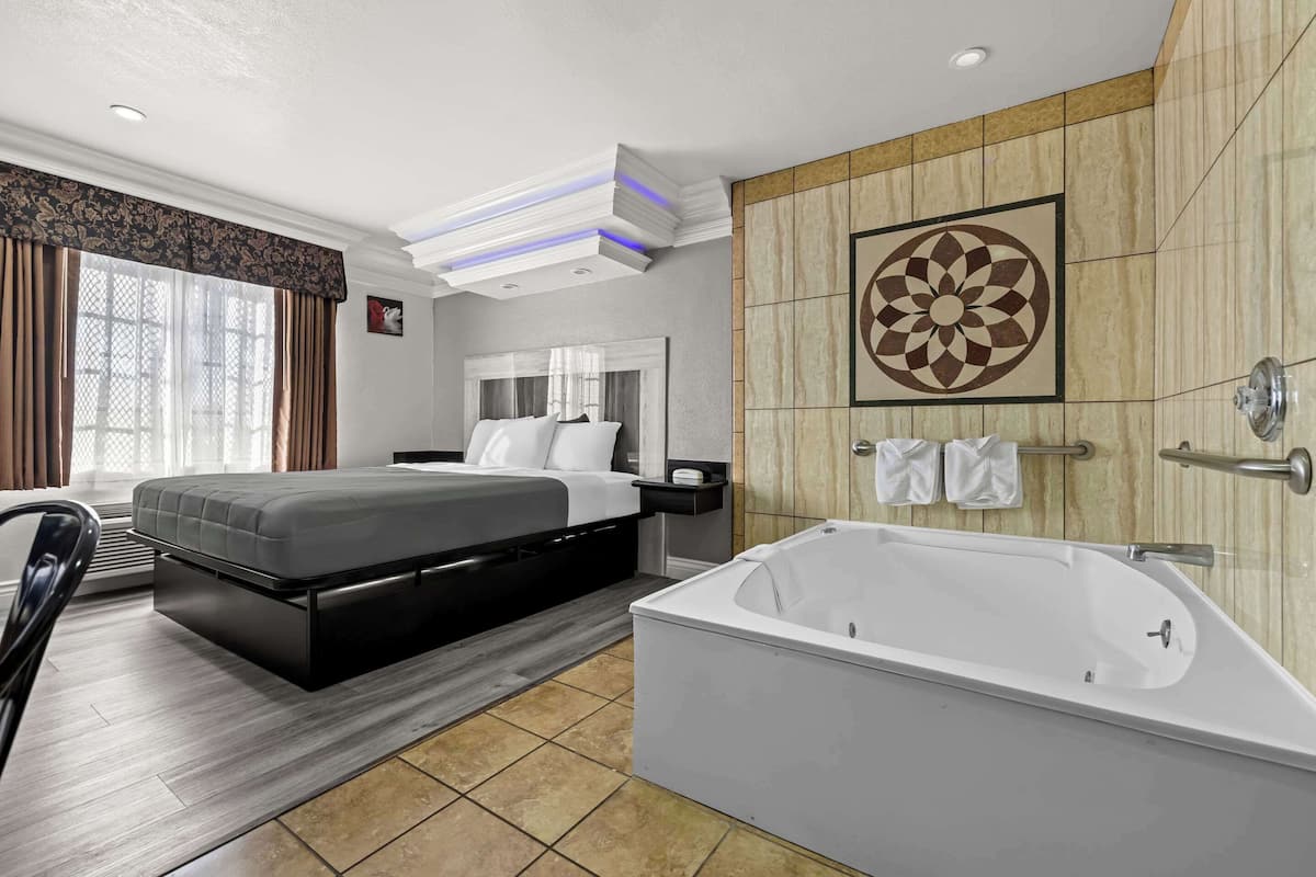A modern hotel room with a large bed, a separate sitting area, a bathtub, and a decorative wall panel.
