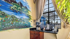 A kitchen with a coffee machine, a window with curtains, and a mural on the wall. - Rodeway Inn Santa Ana - Garden Grove (Santa Ana)
