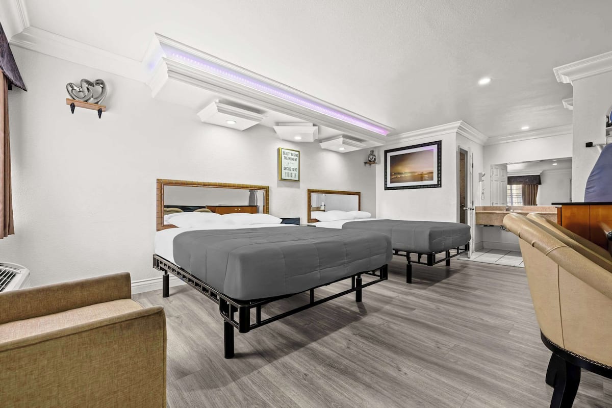 A hotel room with two beds, a sofa, a TV, and a bathroom visible through an open door.
