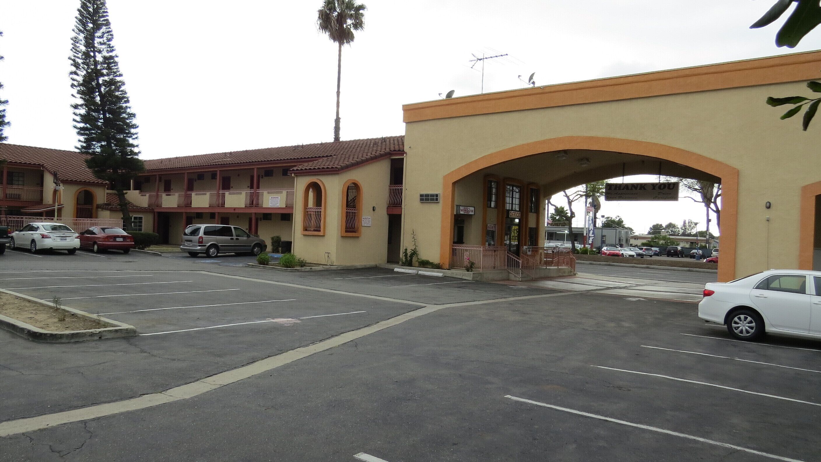A parking lot with several cars, a building with a red-tiled roof, and an archway entrance.