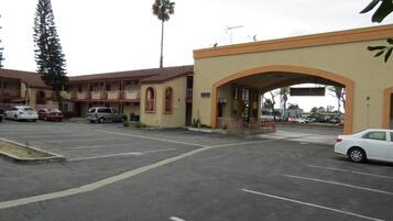 A parking lot with several cars, a building with a red-tiled roof, and an archway entrance.