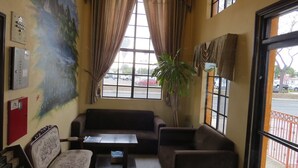 A room with a large window, a sofa, a chair, a small table, and a plant. - Rodeway Inn Santa Ana - Garden Grove (Santa Ana)