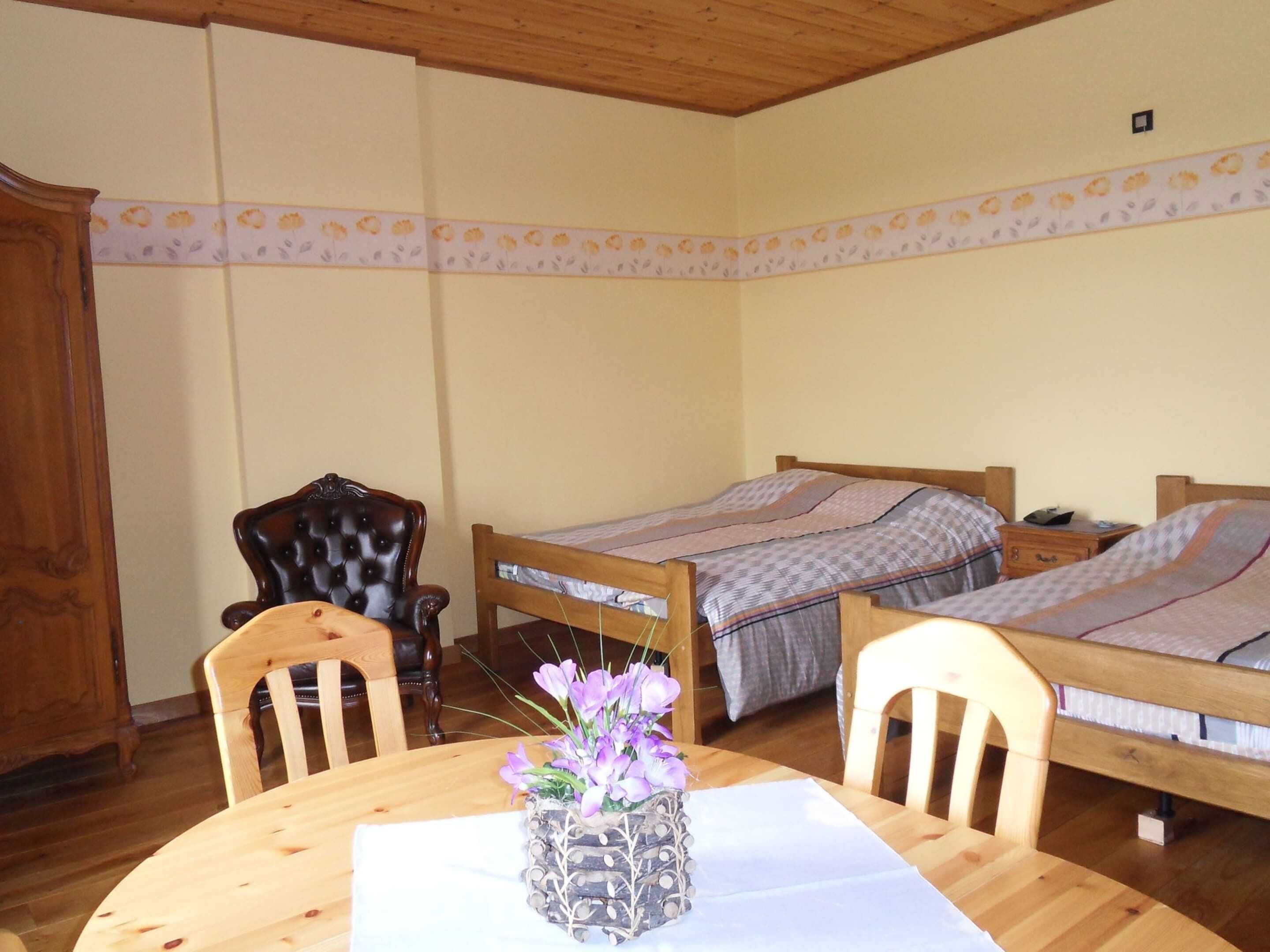 A room with two wooden beds, a wooden dining table with chairs, and a decorative vase with flowers.