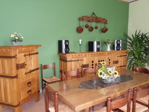 A dining area with a wooden table, chairs, a cabinet, and a wall-mounted speaker system.