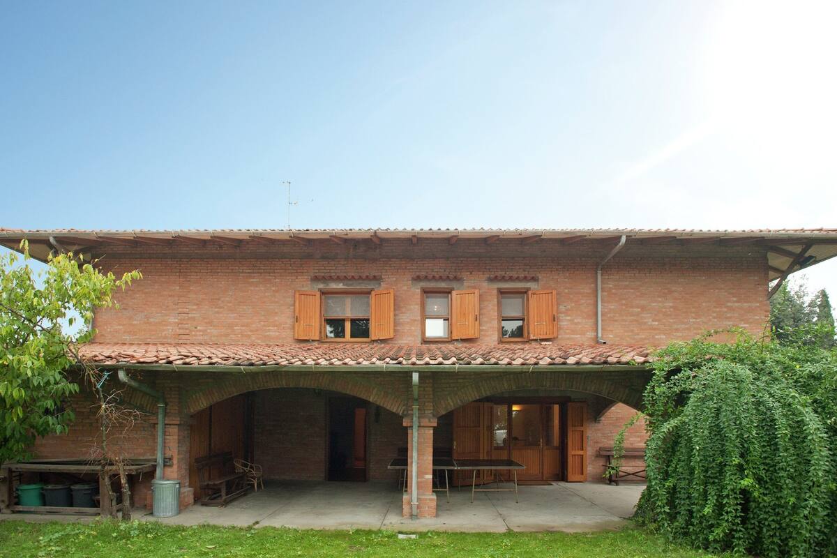 Un edificio de ladrillo con techo de tejas, contraventanas de madera y un patio cubierto.