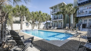 A pool area with lounge chairs, palm trees, and a multi-story building with balconies.