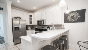 A modern kitchen with white cabinetry, stainless steel appliances, and a central island with bar stools.