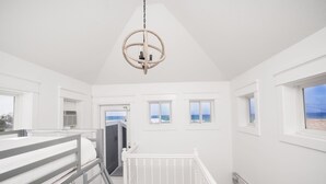 A bright, white room with a bunk bed, a hanging light fixture, and a view of the sea through a window.