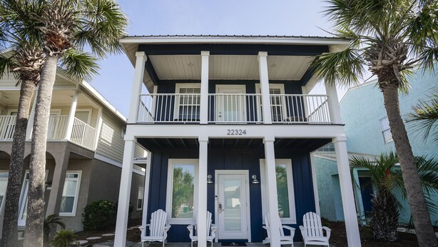 A two-story house with a balcony, numbered 22324, featuring a front porch with white chairs and a door.