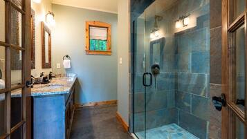 A bathroom with a glass-enclosed shower, a vanity with a marble countertop, and a window with a view.