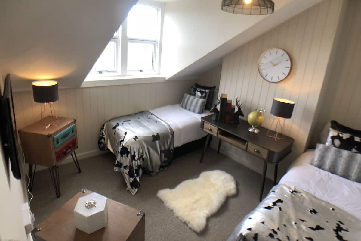 A bedroom with a bed, a desk, a dresser, a clock, and a window.