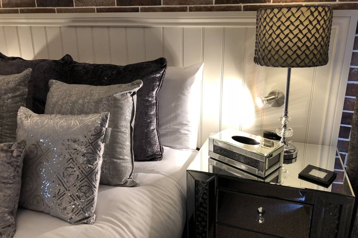 A bed with multiple pillows, a bedside lamp, and a small table with a tissue box and a remote control.