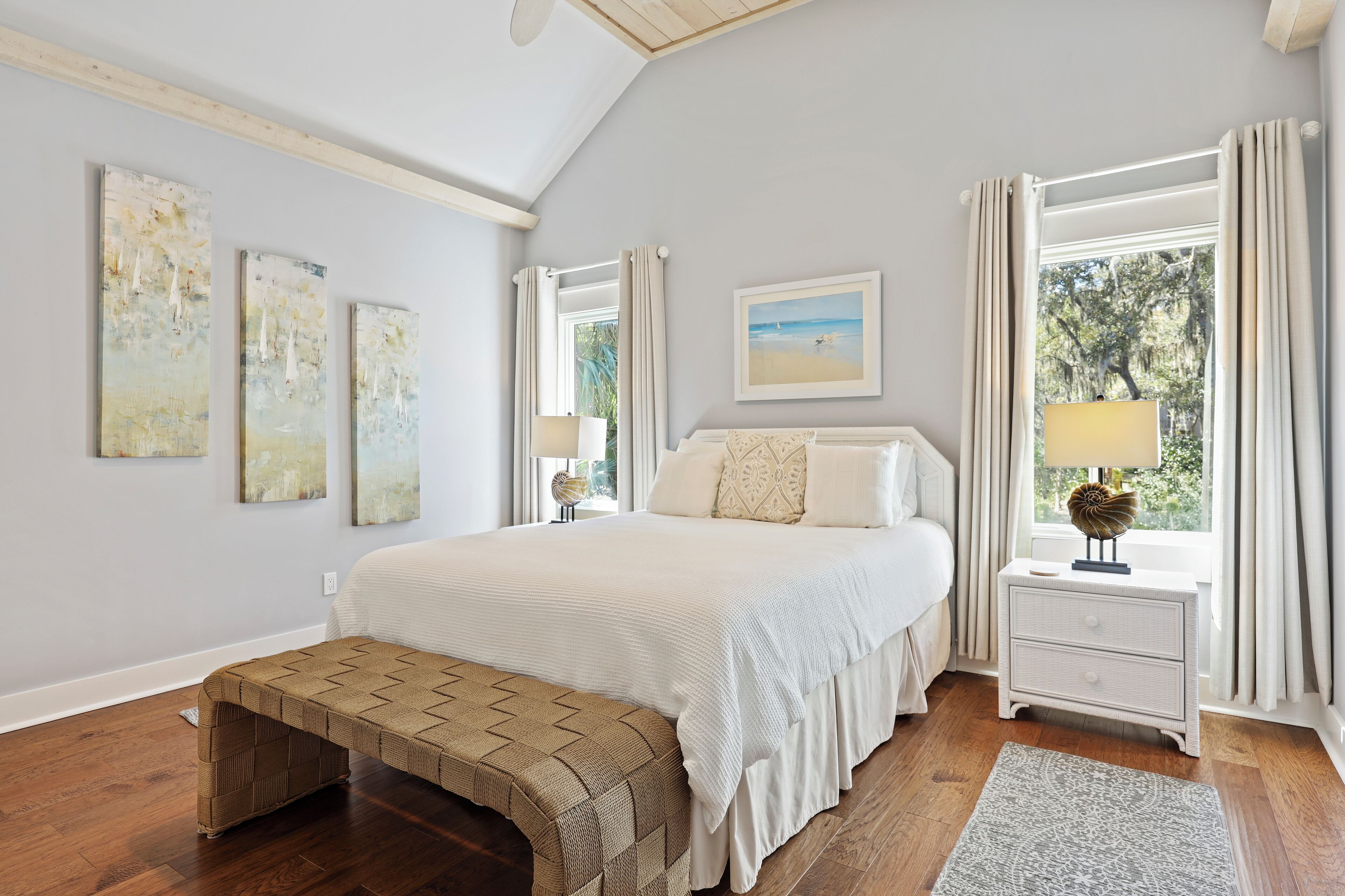 A bedroom with a large bed, a bench, a nightstand, and a window with curtains.