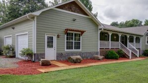 A single-story house with a front porch, a garage, and a stone foundation. - Deep Creek, Lg Yard, Porch Deck, Covered Parking, mile from EVERYTHING (Bryson City)