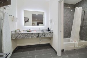 Un baño moderno con encimera de granito, un espejo grande, una ducha con cortina y un perchero para toallas.