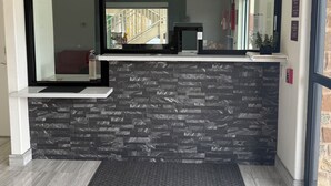 A reception area with a stone wall, a reception desk, and a glass door leading to a staircase. - REGENCY INN AND SUITES (Humble)
