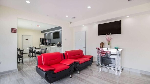 A modern living area with a red sofa, a dining table with chairs, a kitchen area, and a mounted TV. - REGENCY INN AND SUITES (Humble)