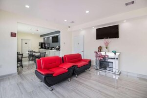 Un espacio habitable moderno con un sofá rojo, una mesa de comedor con sillas, una zona de cocina y un televisor montado.