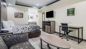 A modern hotel room with a bed, sofa, desk, and TV. - REGENCY INN AND SUITES (Humble)