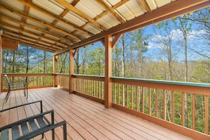 Une terrasse en bois couverte, dotée de rampes, de bancs et offrant une vue sur les arbres.