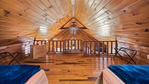 Une cabane en bois avec un plafond en pente, une poutre centrale en bois, un petit escalier et une vue par la fenêtre.