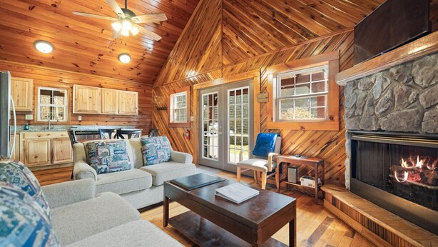 L’intérieur d’une cabane en rondins, avec une cheminée, un plafond en bois et un coin salon accueillant, comprenant un canapé et une table basse.