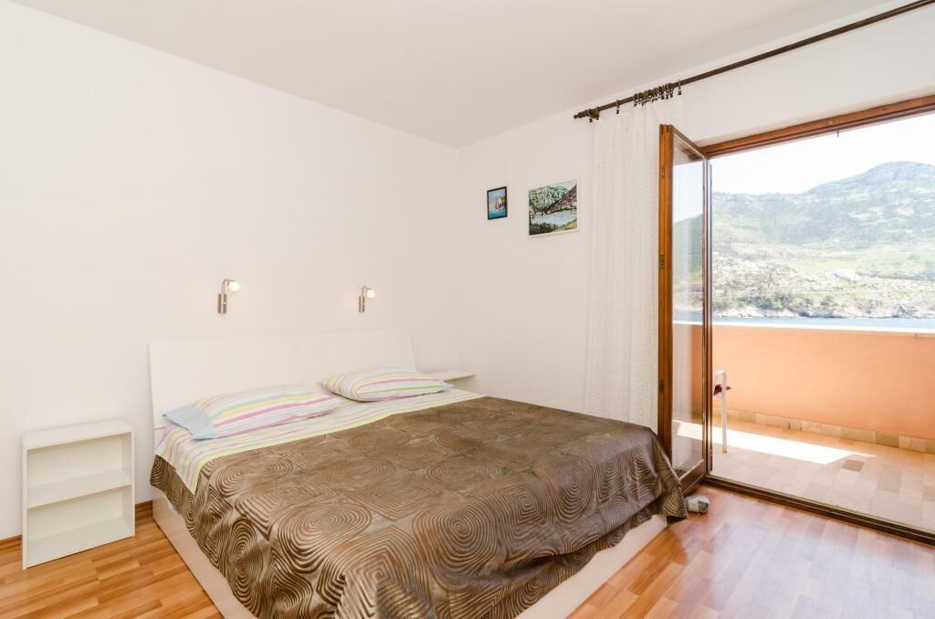 Ein Schlafzimmer mit Bett, einem kleinen Nachttisch, einem Fenster mit Landschaftsblick und einer Tür zu einem Balkon.