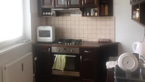 Una cocina compacta con armarios de madera oscura, un microondas blanco, una estufa a gas y un horno pequeño.