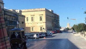 Vista callejera con un edificio, coches aparcados y un carruaje tirado por caballos.