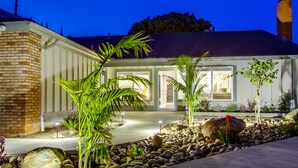A modern house with a brick facade, a covered patio area with plants, and a well-lit entrance. - Spacious home with incredible backyard views (San Diego)
