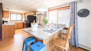 Una cocina moderna con armarios de madera, encimera de granito, taburetes de bar azules y un comedor con una silla de madera.