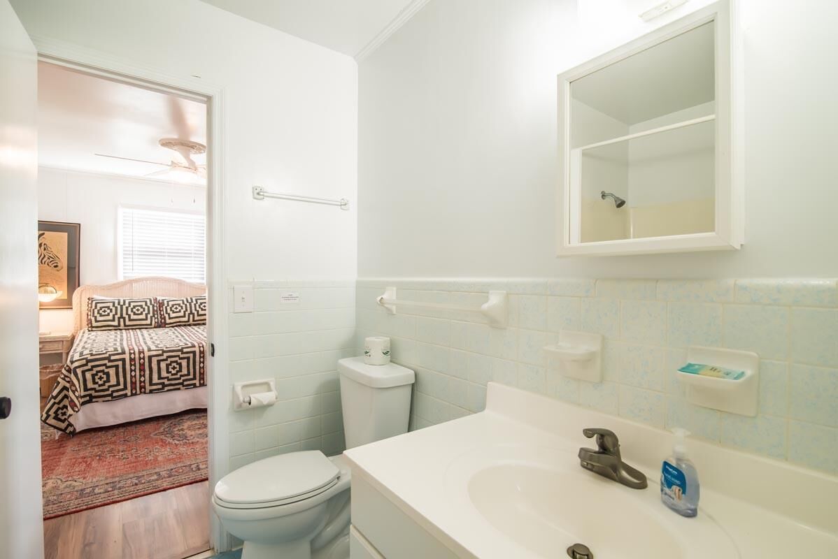 A small, clean bathroom with a toilet, sink, and mirror. There is a towel rack and a soap dispenser on the wall.