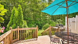 A wooden deck with a grill and outdoor table, surrounded by lush greenery. - Fully stocked vacation home with large private yard, decks and BBQ gas grill & 1 mile to Narragansett Beach ! (Narragansett)