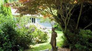 A garden with a statue, a pond, and a house in the background. - Fully stocked vacation home with large private yard, decks and BBQ gas grill & 1 mile to Narragansett Beach ! (Narragansett)