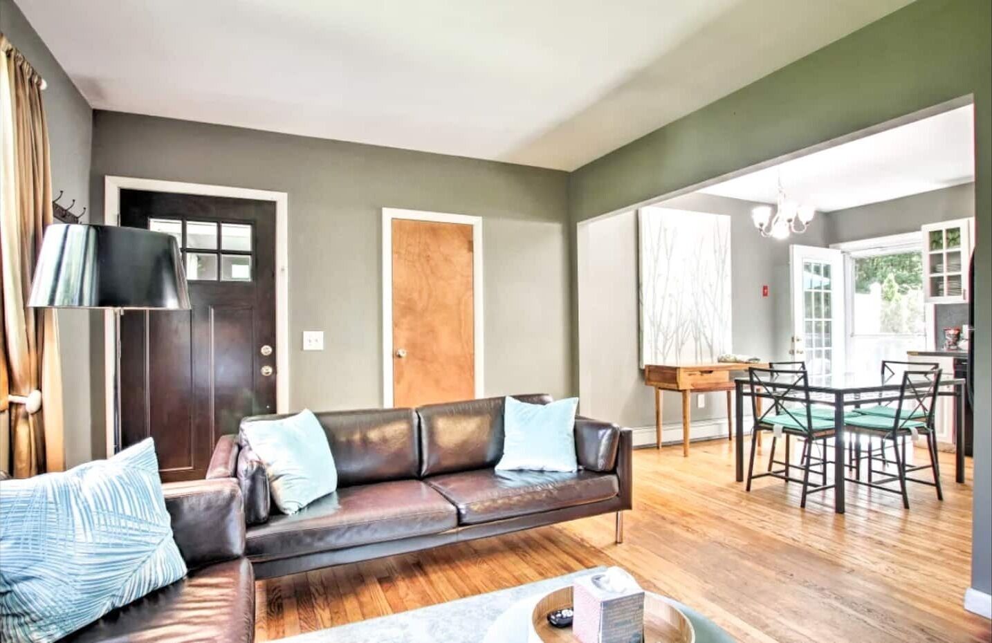 A living room with a dark brown leather sofa, a wooden coffee table, and a dining area with a glass table and chairs.