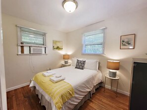 Een hotelkamer met een bed, twee nachtkastjes, twee lampen, een schilderij en een raam met jaloezieën.