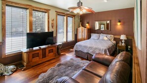 Une chambre à coucher avec un grand lit, une télévision, une armoire en bois et un ventilateur de plafond.