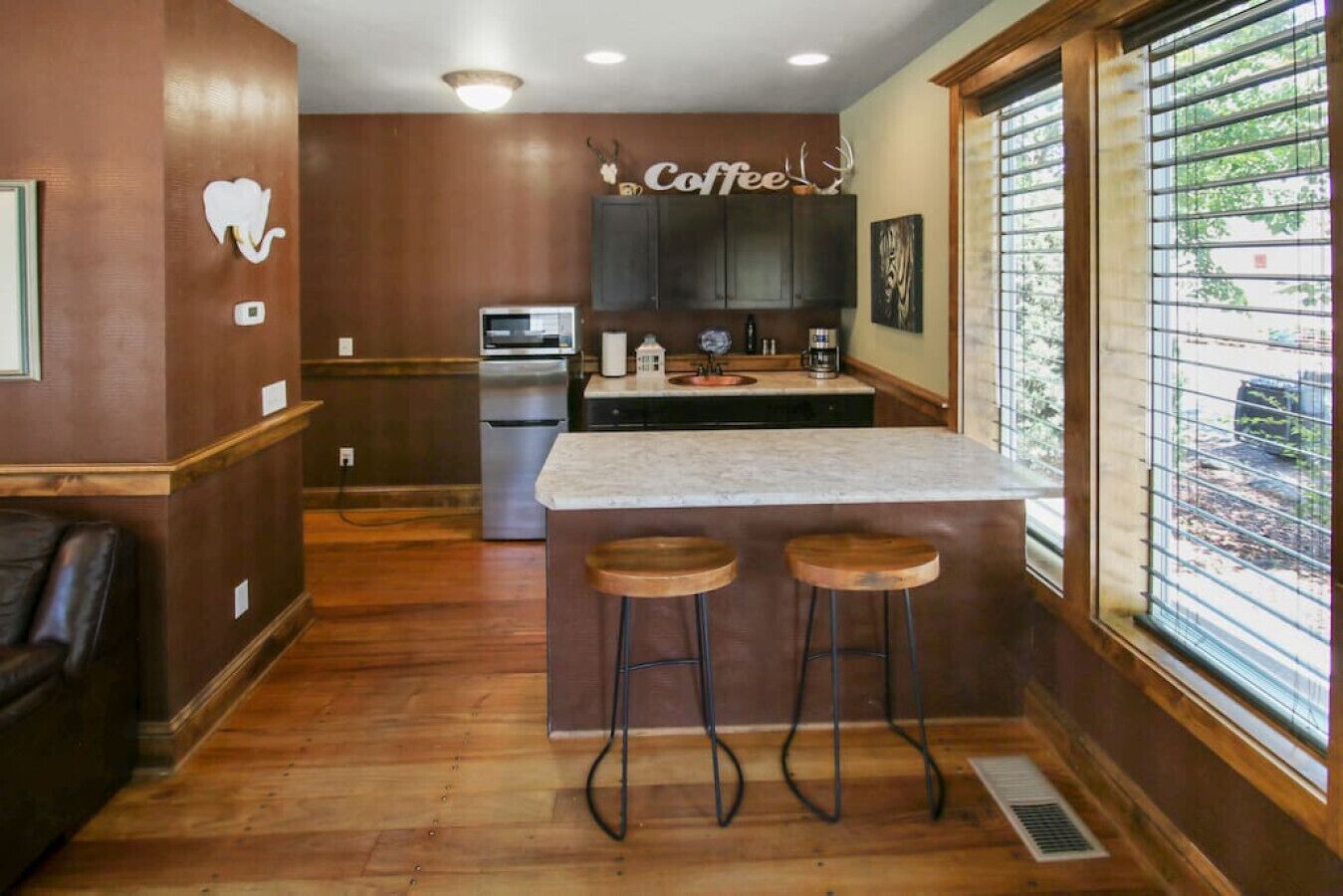 Una cocina con una isla central, taburetes de madera y un ventanal con persianas.