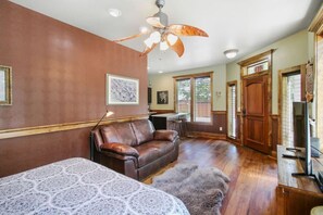 A spacious living room with a brown leather sofa, a patterned table, a ceiling fan, and a view of the outdoors through large windows.