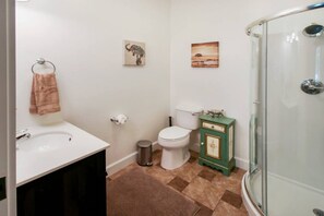 A bathroom with a white sink, toilet, and a glass shower enclosure. There are two wall-mounted pictures, one of an elephant and another of a landscape.