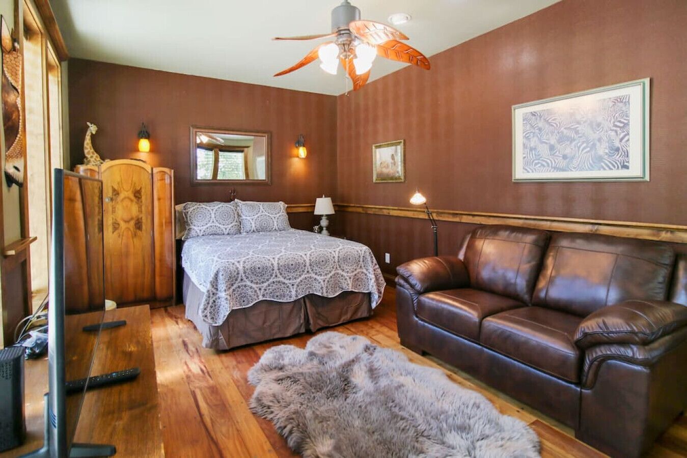 Ein Schlafzimmer mit einem Bett, einem Ledersofa, einem Fellteppich, einem Holzschrank und einem Deckenventilator.