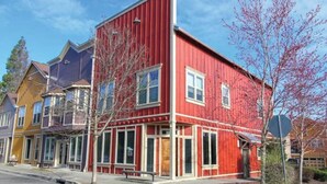 Une rangée de maisons de ville aux couleurs vives, dont une rouge au premier plan, avec de grandes fenêtres et un porche à l’avant.