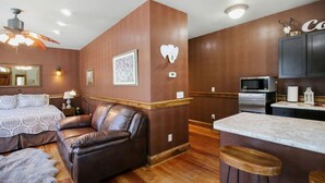 Une chambre d’hôtel moderne dotée d’un grand lit, d’un canapé en cuir, d’un plancher en bois, d’un coin cuisine avec un four à micro-ondes et d’un tabouret de bar.