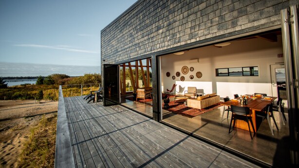 A modern house with a large glass door leading to a dining area with a wooden table and chairs. - Bay Point Landing (Coos Bay)