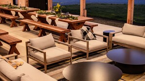 An outdoor patio with wooden furniture, including sofas, benches, and tables, overlooking a body of water. - Bay Point Landing (Coos Bay)