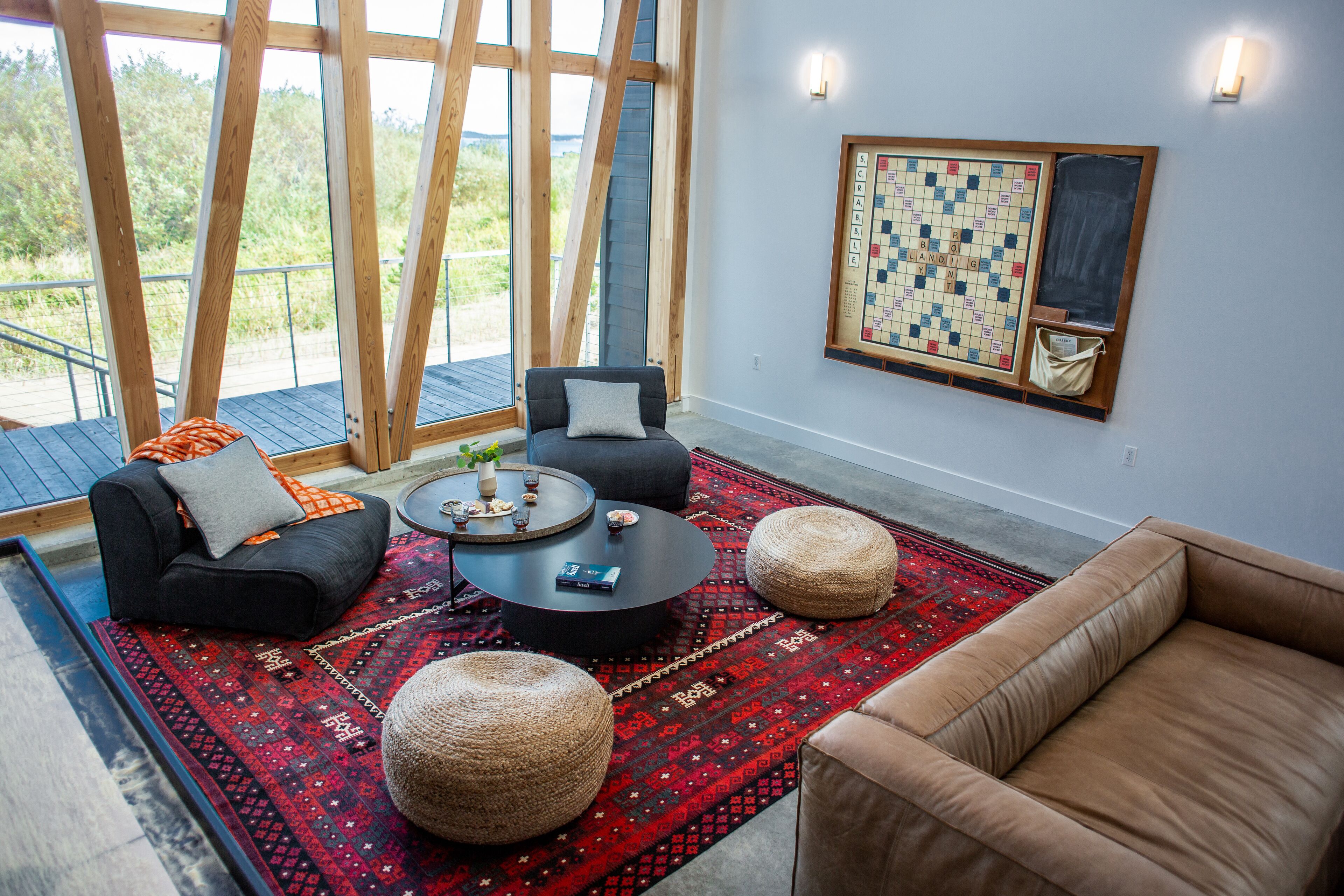 Un salon moderne avec une grande fenêtre, un jeu d’échecs accroché au mur et un tapis rouge à motifs.