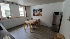 A small kitchen with a wooden table and chairs, a refrigerator, and a window with curtains. - Vacation apartment "Pfalz" - centrally located in Grünstadt (Grünstadt)