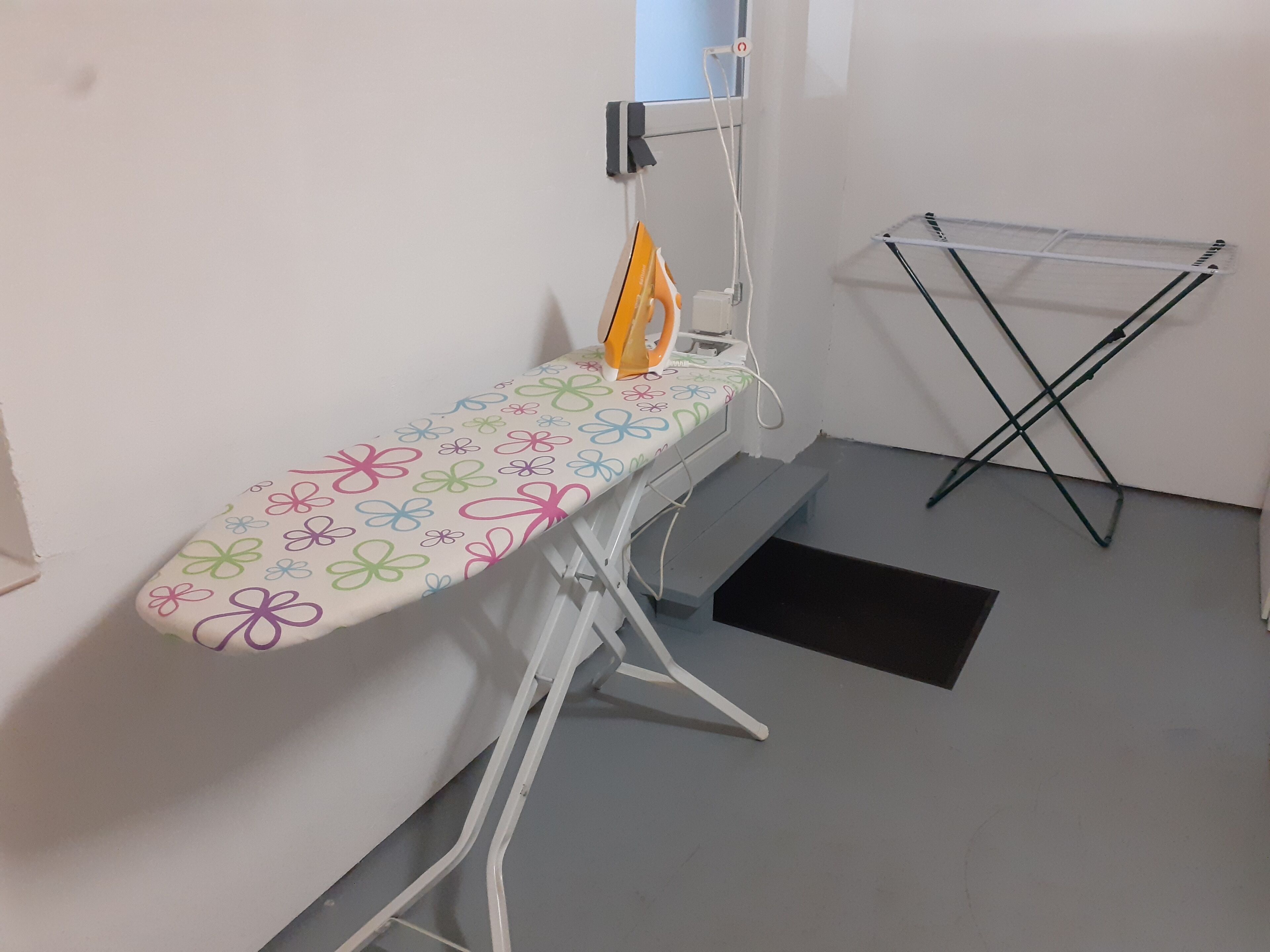 Una tabla de planchar con estampado floral, una tabla de planchar abatible y un tendedero.