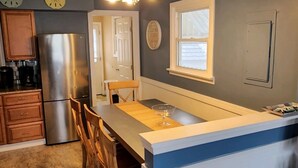 Una cucina con isola centrale, sedie in legno, frigorifero in acciaio inossidabile e un cartello con la scritta 'BEACH HOUSE'.